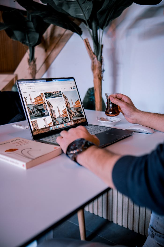 Person sipping tea and browsing on a laptop in a cozy indoor setting.